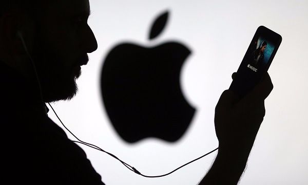 A man checks the Apple Music streaming site using his Apple Inc. iPhone 6s as he stands framed against a wall bearing the Apple logo in this arranged photograph in London, U.K., on Wednesday, Dec. 23, 2015. Beatles songs will now be available around the world on nine streaming services including Apple, Spotify, Deezer and Google Play, the bands record company, Vivendi SAs Universal Music Group, said Wednesday in a statement. Photographer: Chris Ratcliffe/Bloomberg